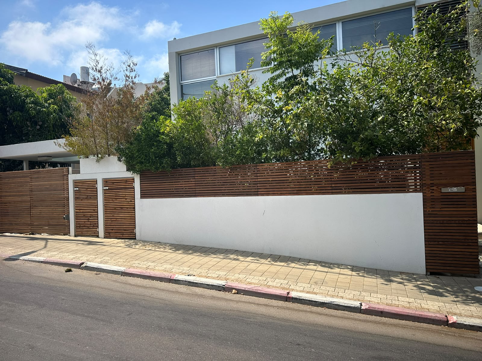 גדר עץ מעוצבת עם דלתות כניסה מעל קיר לבן